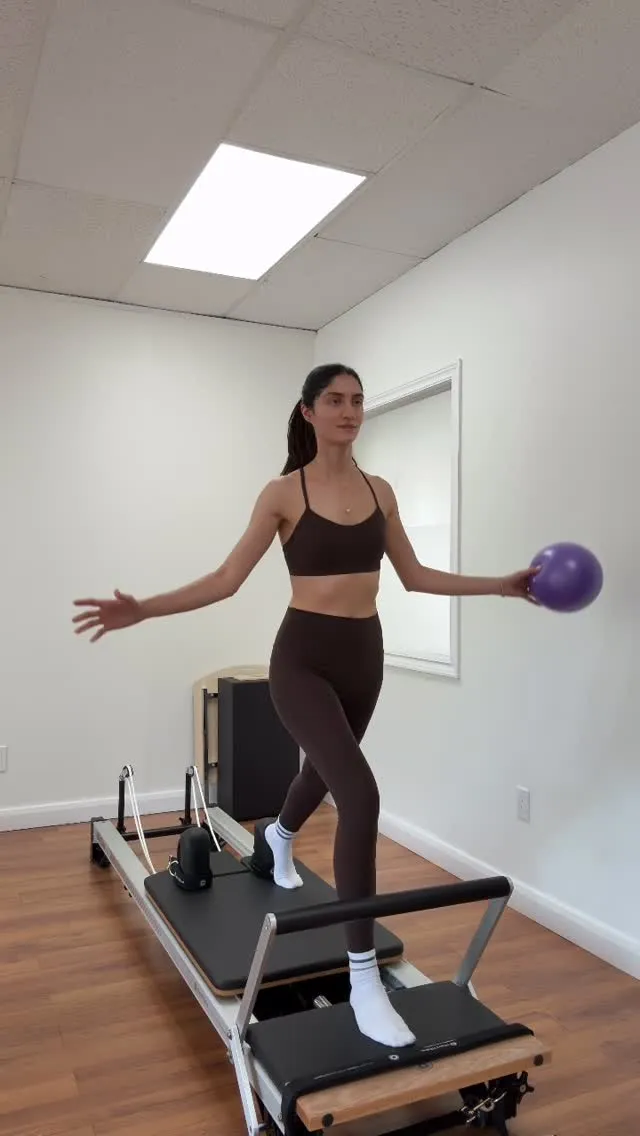 Toktam balancing on the reformer, holding a small ball out to the side
