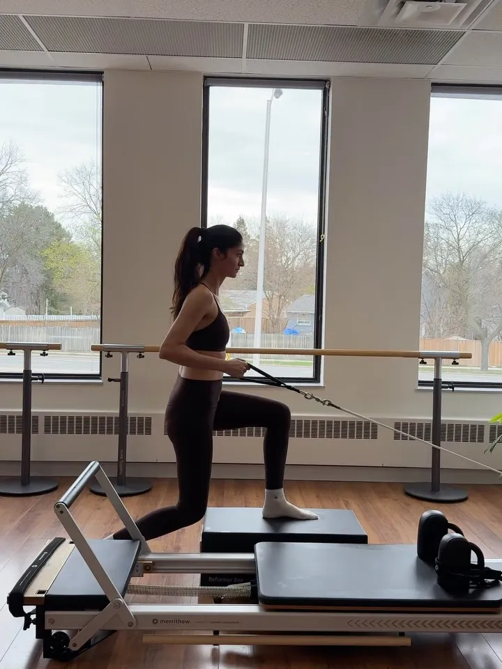 Toktam in a standing lunge on the reformer, holding the straps